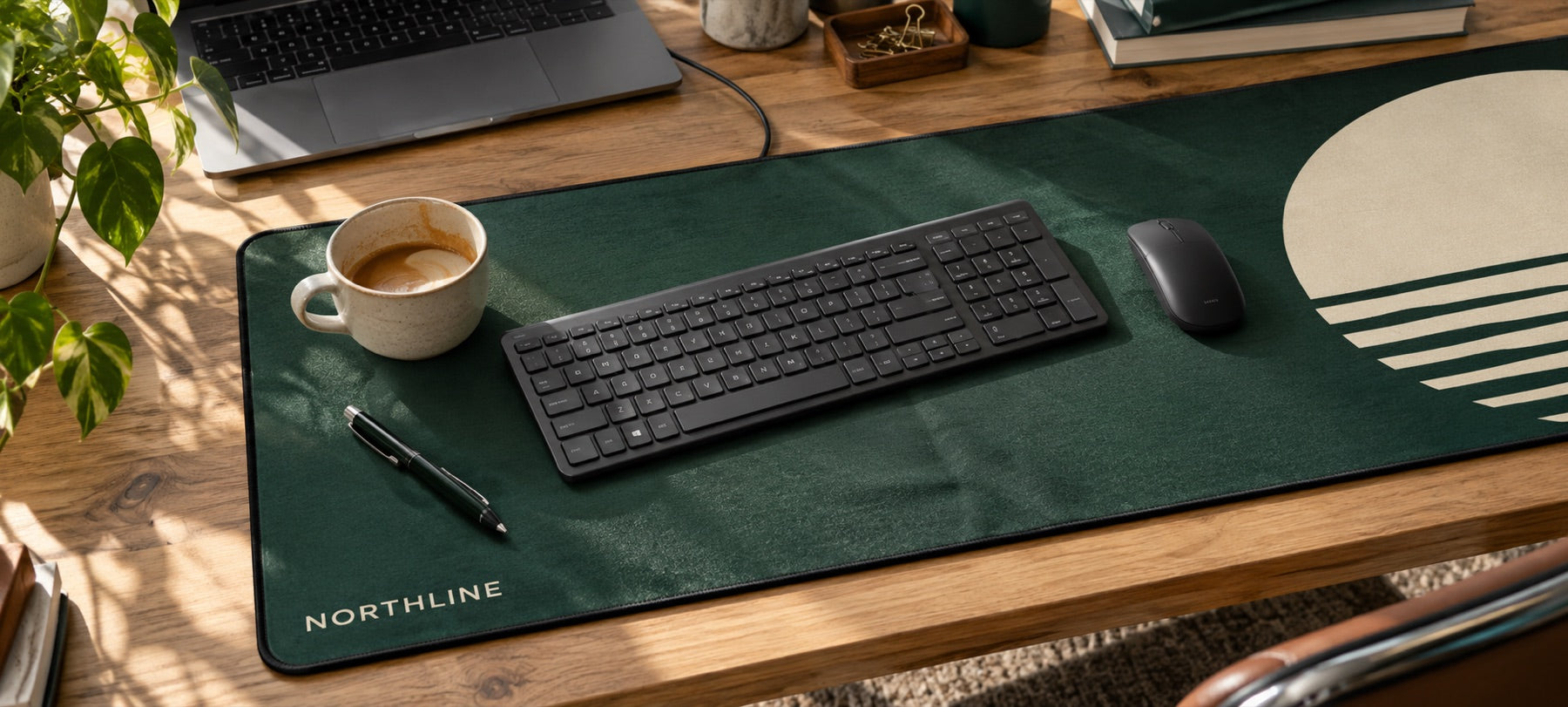 A long desk mat printed with a green and cream coffee-brand design on an oak desk